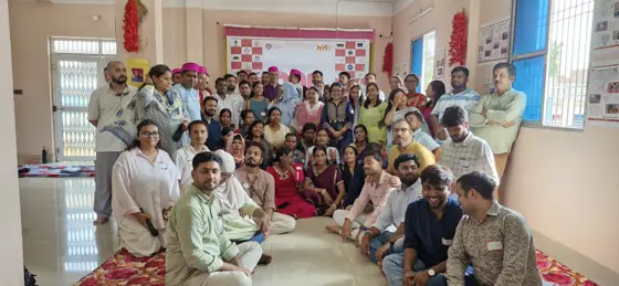 A large group of people posed together in a hall, some seated on the floor.