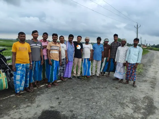 A group of workers standing together on a road beside paddy fields.