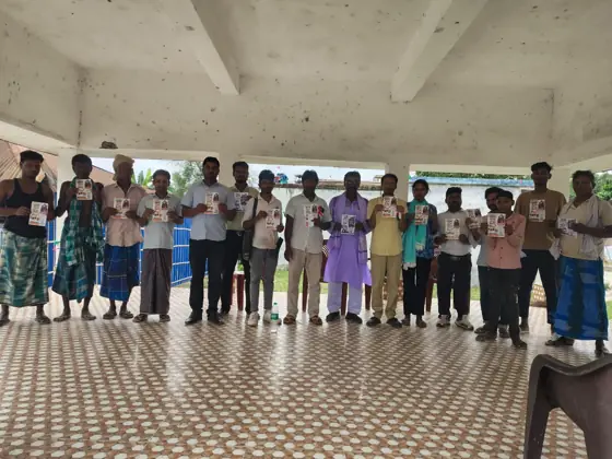 Workers in a line holding leaflets in an open hall.
