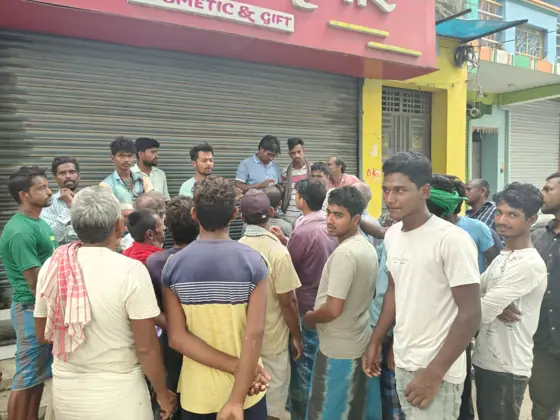 A crowd of men gathered outside a shuttered shop.