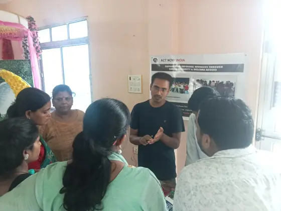 A man speaking to women and men beside an Act Now India poster.