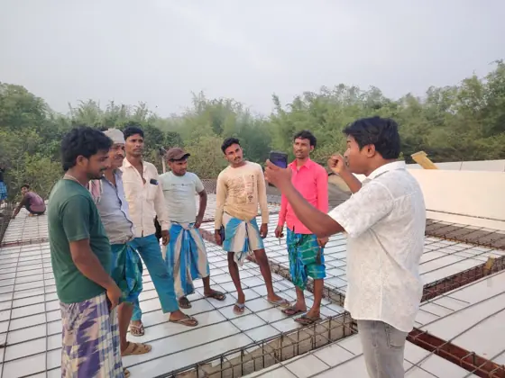 A man speaking to a group of workers on an unfinished concrete roof.