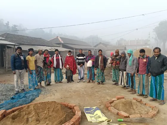 Men standing in a circle on open ground in a village in morning mist.